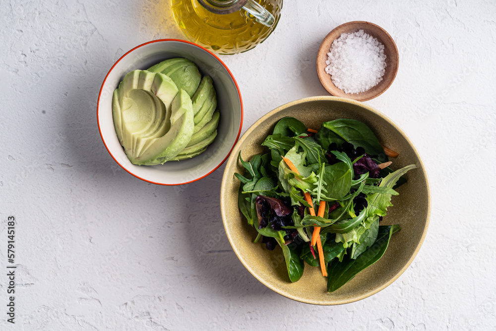 Obraz premium Salad ingredients leaf vegetables and sliced avocado in bowls on white background