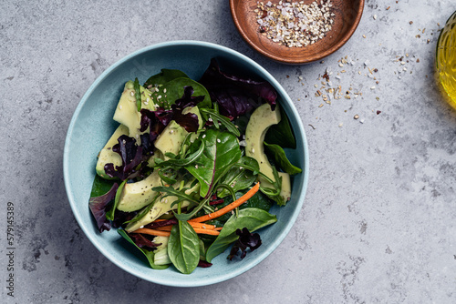 Salad with leaf vegetables and sliced avocado in bowl on grey background