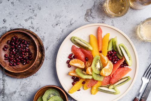 Bowls with fresh fruits (grapefruits, tangerines, pomegranate seeds, oranges, and kiwi), preparing fruit salad, ingredients