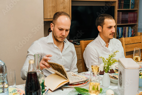 Passover Seder.Two Men Celebrate Passover with Traditional Foods, and Reading Haggadah. Jewish Family At The Table Celebrating Pesach. Young Bearded Man Reads The Passover Haggadah. photo