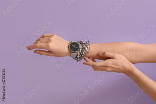 Woman with stylish wristwatch and bracelet on lilac background photo