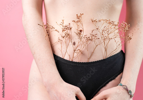 A slender woman in underwear holds a sprig of dried flowers near the intimate area. Close-up. The concept of hair removal and skin care.