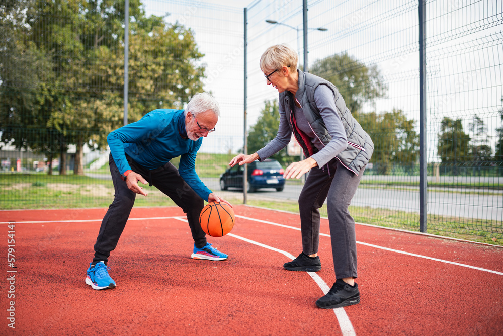 Cheerful active senior couple playing basketball on the urban basketball street court. Happy living after 60.  Active lifestyle pensioners.