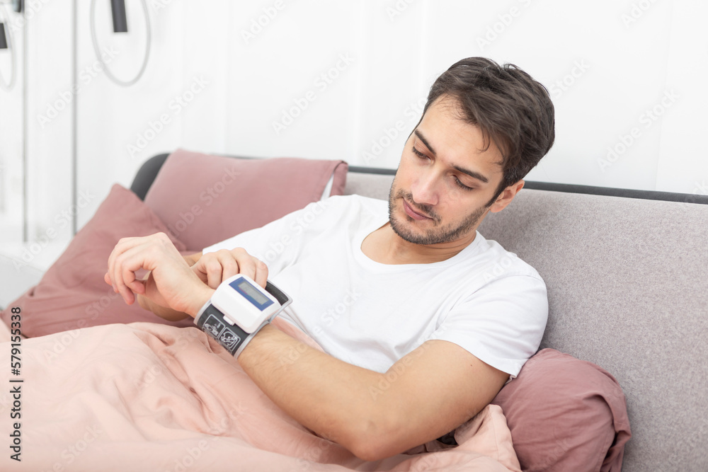 Sick man with wrist blood pressure monitor lying in the bed and