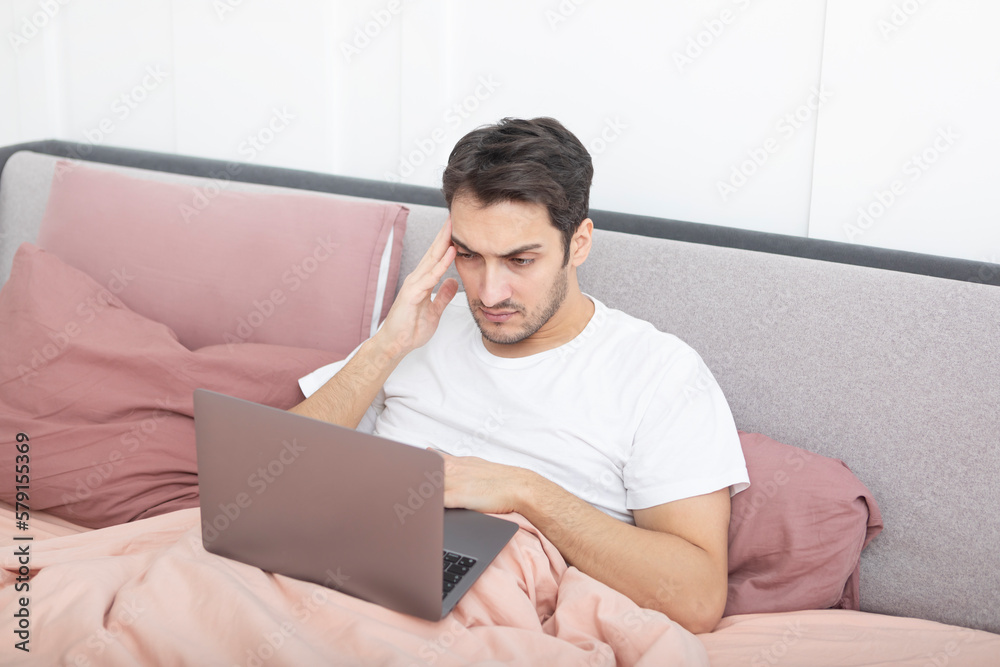 Handsome man lying on the bed and working on laptop in the bedroom Handsome man lying on the bed and working on laptop in the bedroom