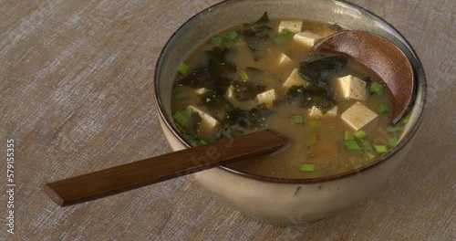 Authentic miso soup with kombu dashi, tofu, wakame seaweed and scallions in a bowl with spoon. Table spin.