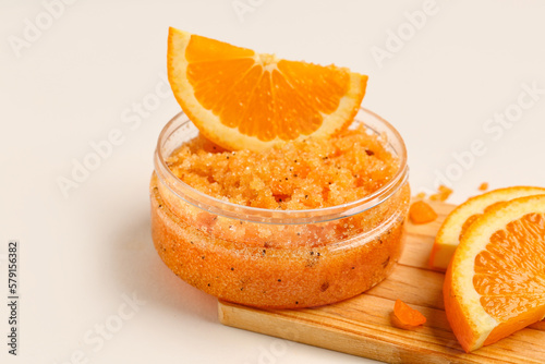 Wooden board with jar of natural body scrub and orange slices on light background, closeup
