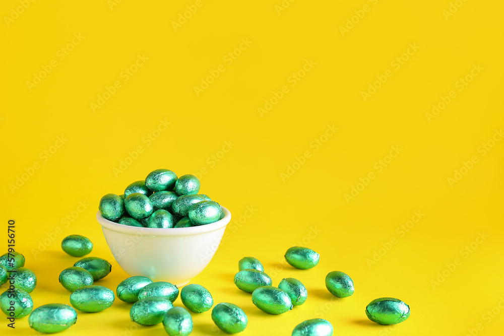 Bowl of chocolate Easter eggs in color foil on yellow background Bowl of chocolate Easter eggs in color foil on yellow background