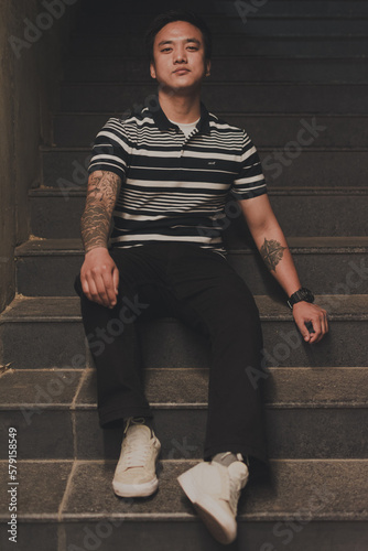 Asian man sitting on stairs - Asian man having tattoos on his arms 