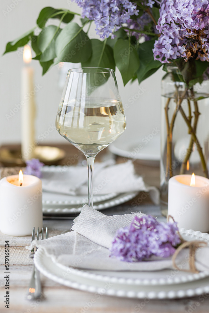 Beautiful table decor for a wedding dinner with a spring blooming lilac flowers. Celebration of a special holiday marriage event. Fancy white plates, wineglasses, candles. Countryside style