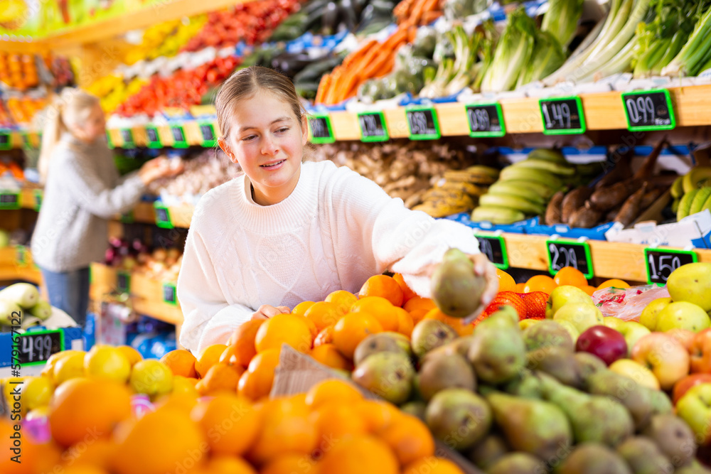 Happy smiling teenage girl making purchases in supermarket, choosing fresh ripe fruits