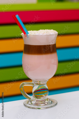 Coffee cocktail with foam and coconut flakes with two straws. Colorful and striped background.