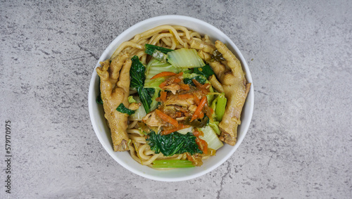 Mie ayam, bakmi ayam, or chicken noodle is a common Indonesian dish of seasoned yellow wheat noodles topped with diced chicken meat and chicken feet photo
