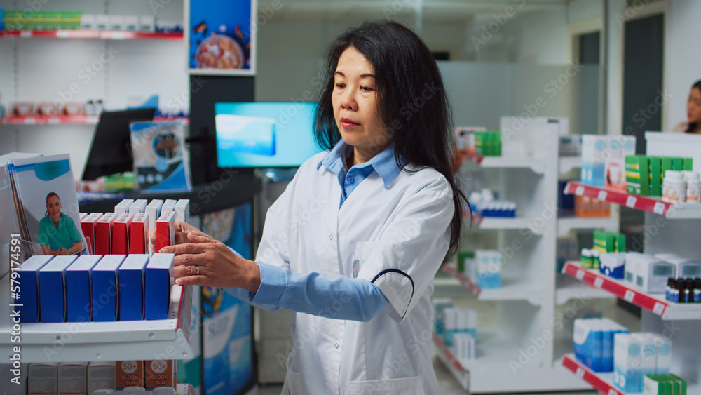 Female consultant looking at cardiology drugs on shelves, working with medical products and pills at shop. Pharmaceutical worker reading boxes of medicaments in pharmacy retail store.
