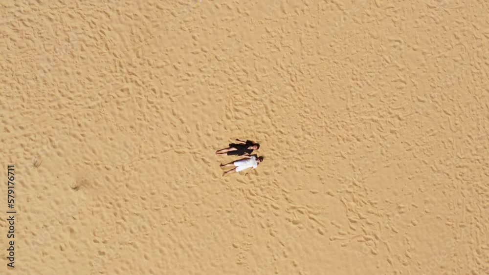 Aerial view of a young couple lying on the white sand. man and woman spend time together and travel through the desert. Aerial view of a young couple lying on the white sand. man and woman spend time together and travel through the desert.