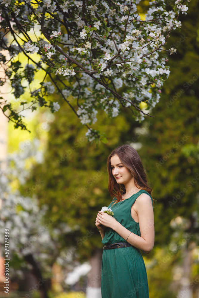 Woman-spring. Young woman in long green dress in a blooming apple garden. Spring story. Brown-haired girl with long hairs. Woman-spring. Young woman in long green dress in a blooming apple garden. Spring story. Brown-haired girl with long hairs.