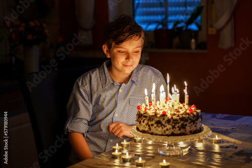 Adorable happy blond little kid boy celebrating his birthday. Preteen child blowing candles on homemade baked cake  indoor. Birthday party for school children  family celebration  teenager birthday