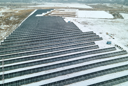 Aerial view of electrical power plant with solar panels covered with snow melting down in winter end for producing clean energy. Concept of low effectivity of renewable electricity in northern region