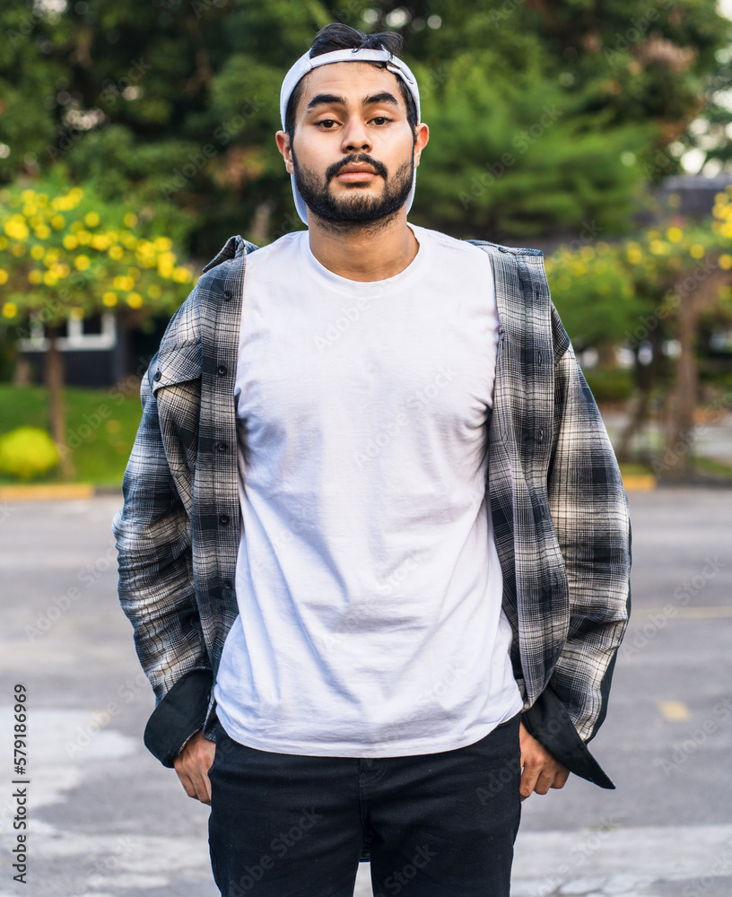 This image features a bearded man striking a confident pose in a white blank shirt, embodying modern masculinity and style This image features a bearded man striking a confident pose in a white blank shirt, embodying modern masculinity and style