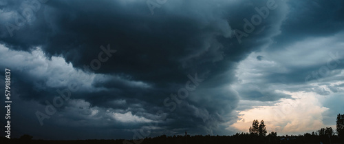 Dramatic cloudscape. Sunny light through dark heavy thunderstorm clouds before rain. Overcast rainy bad weather. Storm warning. Natural blue background of cumulonimbus. Sunlight in stormy cloudy sky.