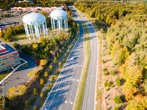 water tower near the road in a small town in the USA. Drone view. Autumn Forest, road, low-rise buildings.