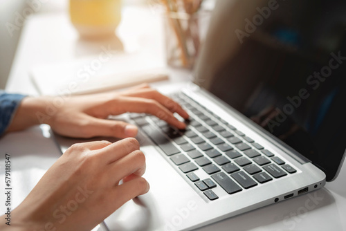 Casual young woman wearing jean shirt, freelance working typing email on laptop at workplace, close up