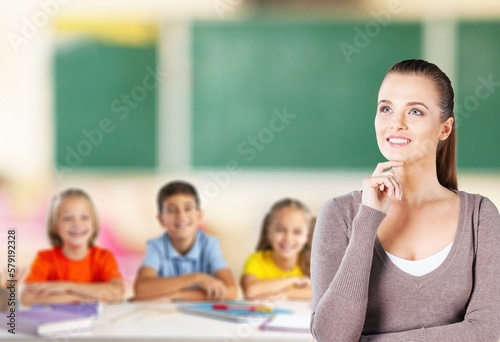 Happy young teacher in class with schoolchild on background.