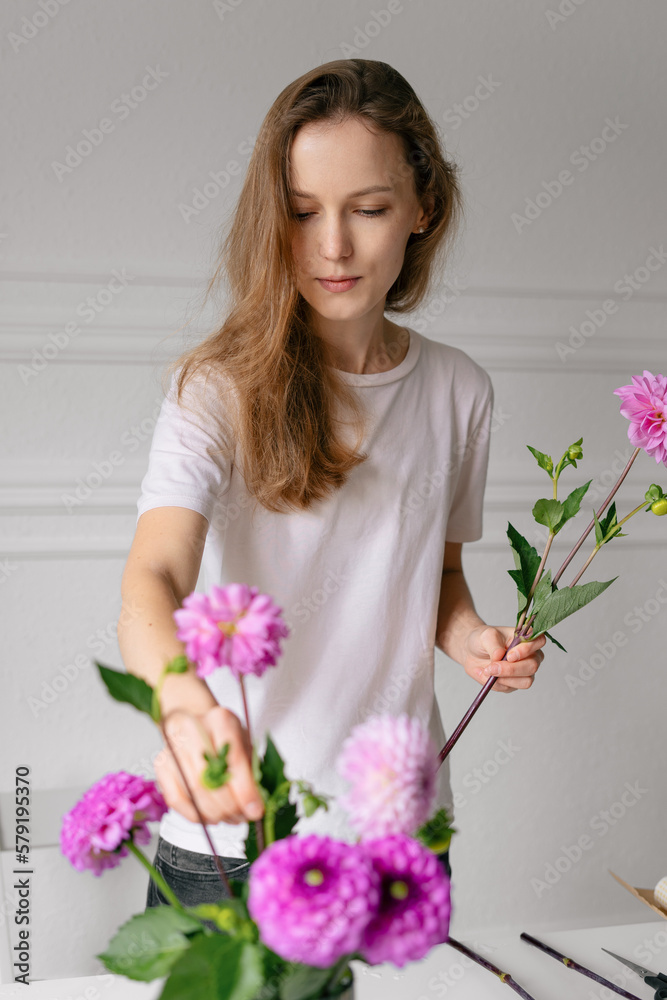A young florist chooses pink flowers for a bouquet, taking them from a vase. Vertical image for your design A young florist chooses pink flowers for a bouquet, taking them from a vase. Vertical image for your design