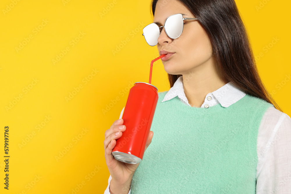 Beautiful woman drinking from red beverage can on yellow background. Space for text Beautiful woman drinking from red beverage can on yellow background. Space for text