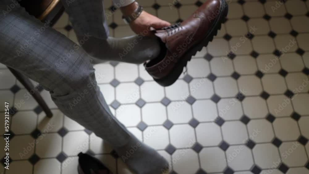 The man puts on his shoes. Male in grey suit and socks laces up his boots. The groom or businessman is getting dressed. The man puts on his shoes. Male in grey suit and socks laces up his boots. The groom or businessman is getting dressed.