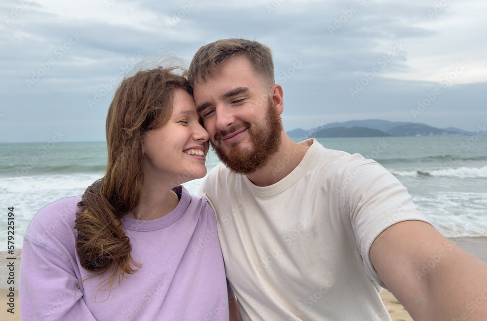 Happy couple in love is enjoy summer vacation on sea, beach take selfie photo, picture of themself on phone, smartphone, hug each other Happy couple in love is enjoy summer vacation on sea, beach take selfie photo, picture of themself on phone, smartphone, hug each other
