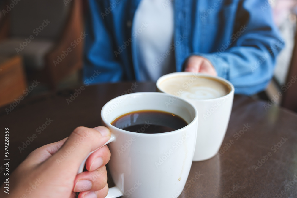 Closeup image of a couple people clinking white coffee mugs in cafe Closeup image of a couple people clinking white coffee mugs in cafe