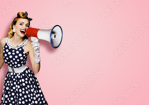 Portrait image of beautiful woman holding mega phone, shout, saying, advertising. Pretty girl in black pin up style dress with mega phone loudspeaker. Isolated rose pink background. Big sales ad.