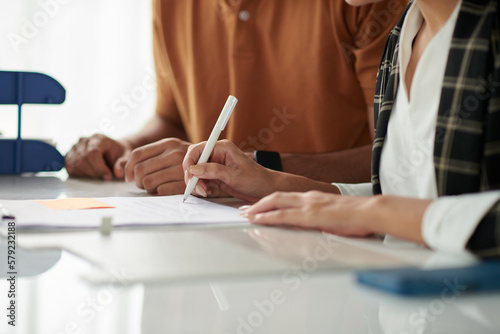 Hands of spouses signing documents at meeting with social worker