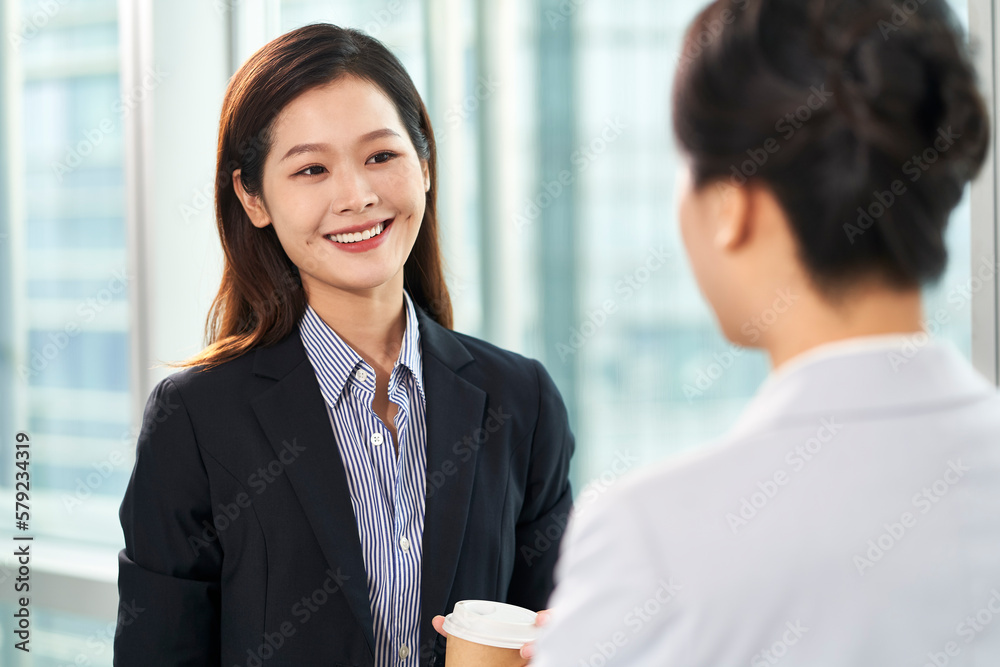 two young asian businesswomen chatting in office two young asian businesswomen chatting in office