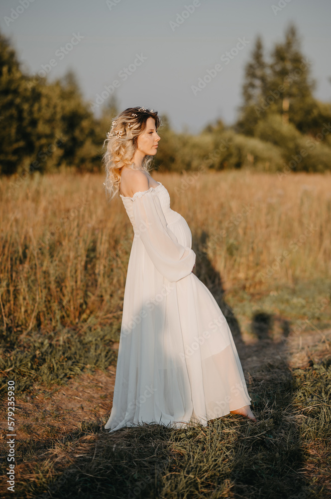 A young expectant mother in the third trimester of pregnancy in a white dress hugs her stomach against the backdrop of a natural landscape. The concept of future motherhood. A young expectant mother in the third trimester of pregnancy in a white dress hugs her stomach against the backdrop of a natural landscape. The concept of future motherhood.