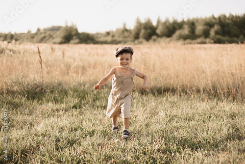 The boy-child is having fun and actively running in the field. A cheerful and sincerely rejoicing boy. Childhood in the countryside.