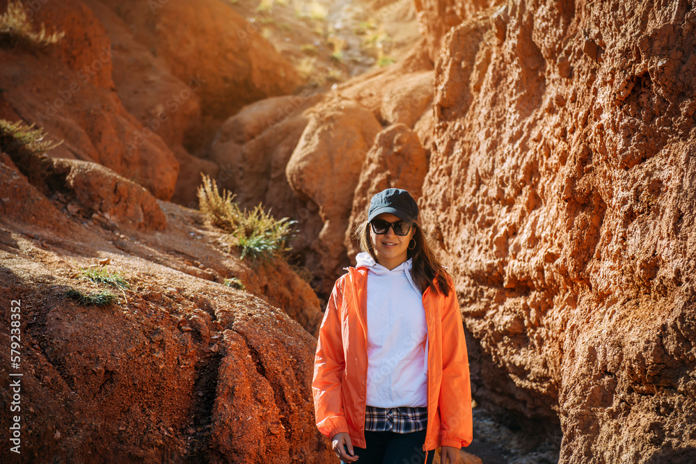 Portrait of impressed woman tourist walking in red sandstone canyon. Young female hiker in mountain trekking. Adventure, wanderlust, sightseeing.