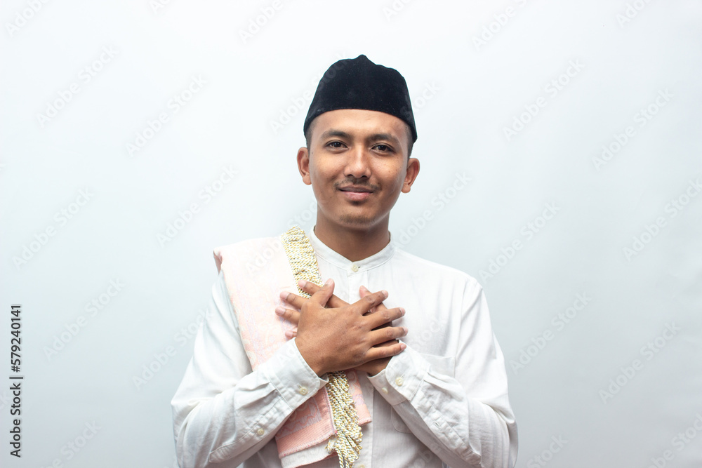 Smiling young Asian man wearing muslim shirt gesturing traditional greeting isolated on white background. Smiling young Asian man wearing muslim shirt gesturing traditional greeting isolated on white background.