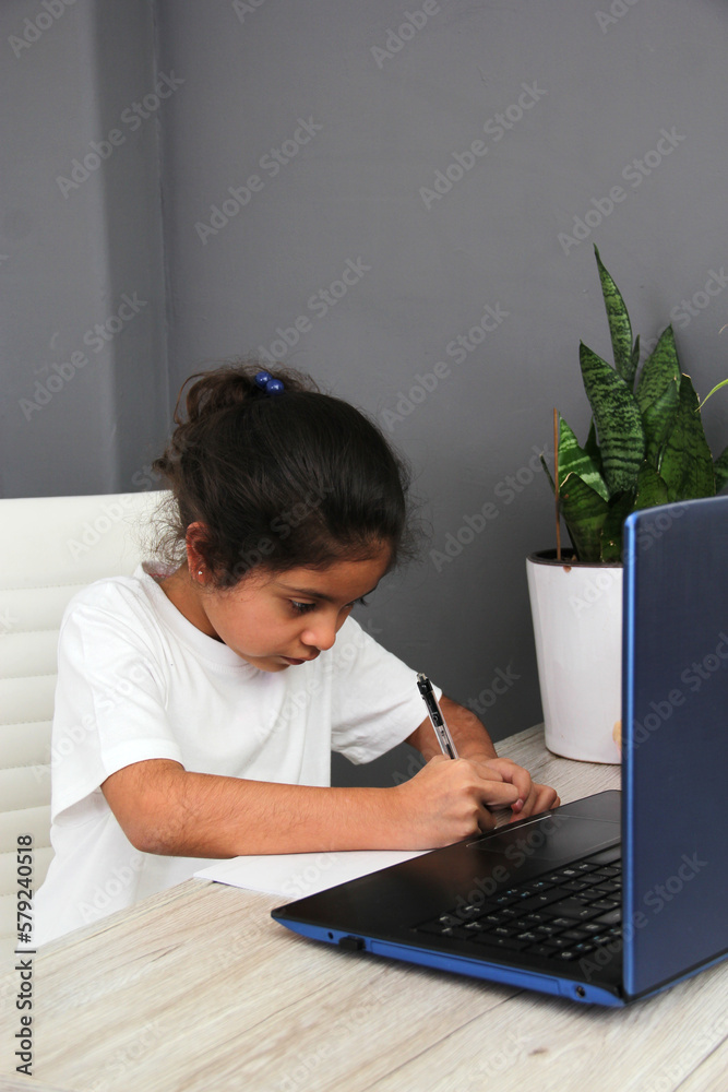 9-year-old Latino girl does home schooling takes online classes at home on a desk with a laptop, studies, is surprised and participates in class 9-year-old Latino girl does home schooling takes online classes at home on a desk with a laptop, studies, is surprised and participates in class