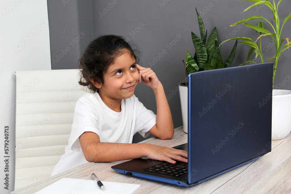 9-year-old Latino girl does home schooling takes online classes at home on a desk with a laptop, studies, is surprised and participates in class 9-year-old Latino girl does home schooling takes online classes at home on a desk with a laptop, studies, is surprised and participates in class
