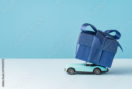 small Luxury gift box with a blue bow on on top of retro toy car. Side view monochrome. Fathers day or Valentines day gift for him. Corporate gift concept or birthday party. Festive sale delivery