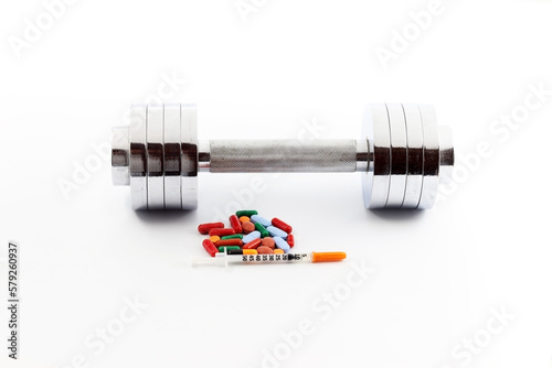 A syringe and steroid tablets or doping substances for athletes, next to gym dumbbells photo