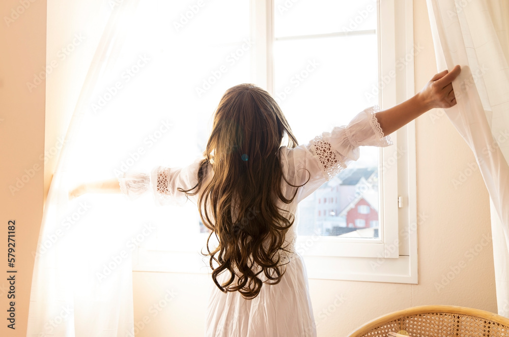 Young woman open a curtains and stretching in bed after waking up, sunlight in morning and open the curtain with lens flare at her home Young woman open a curtains and stretching in bed after waking up, sunlight in morning and open the curtain with lens flare at her home