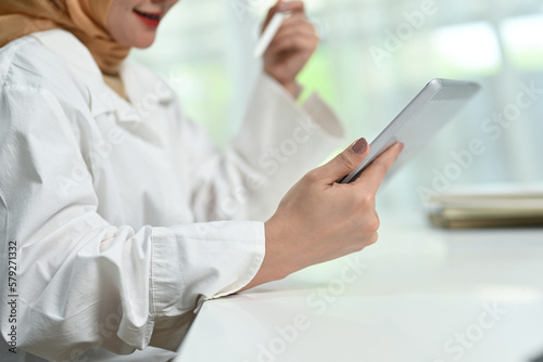 Cropped shot of smiling young muslim woman using digital tablet, enjoying freelance work in home office