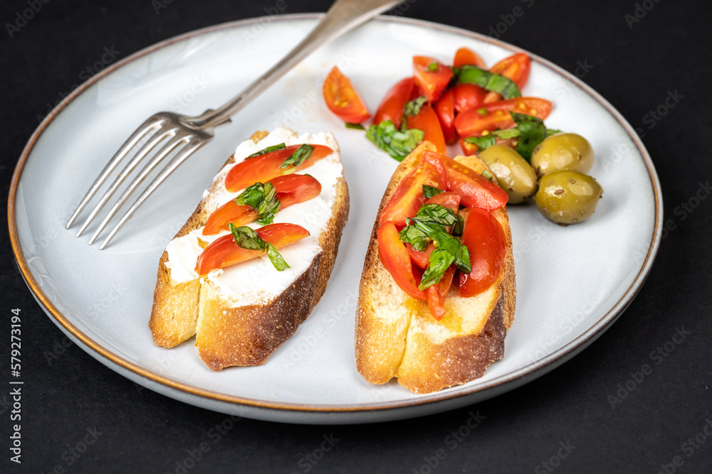 Close up view of tasty bruschettas with cherry tomatoes, cheese, basil and olive oil in a plate on black background. Italian style cuisine.