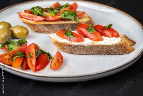 Close up view of tasty bruschettas with cherry tomatoes, cheese, basil and olive oil in a plate on black background. Italian style cuisine.