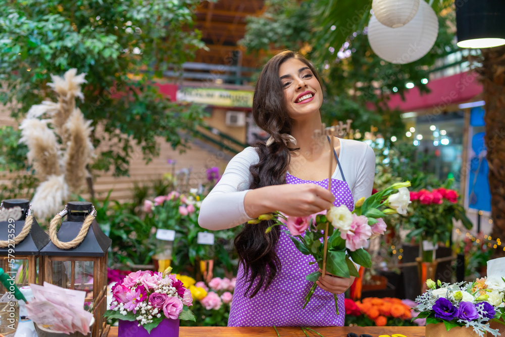 Beautiful florist stands behind a counter in a flower shop and makes a bouquet for a customer