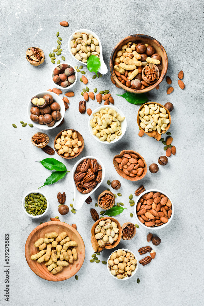 Assortment of nuts in bowls. A variety of peeled nuts on a stone background. Top view. Assortment of nuts in bowls. A variety of peeled nuts on a stone background. Top view.