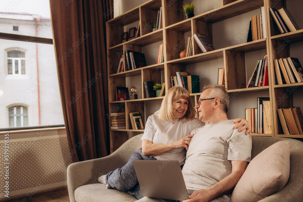 Senior middle aged happy couple embracing using laptop together, smiling elderly family reading news, shopping online at home, older people and computer or good vision after laser correction concept